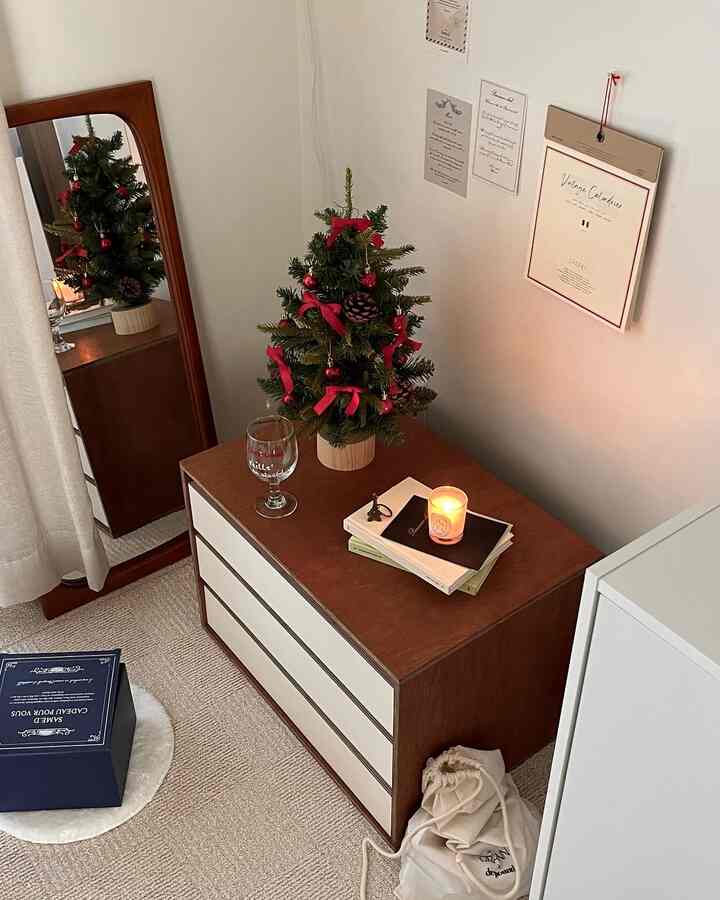 ウッドトーンとレッドが調和する小さな空間、低いチェストの上にクリスマスツリーとキャンドルが置かれ、温かみのあるヴィンテージな雰囲気のインテリア
