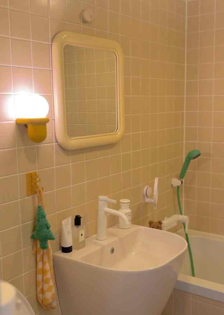 Bathroom with light yellow tiled walls and white sink, featuring a yellow wall lamp and green Christmas garland for cozy mood