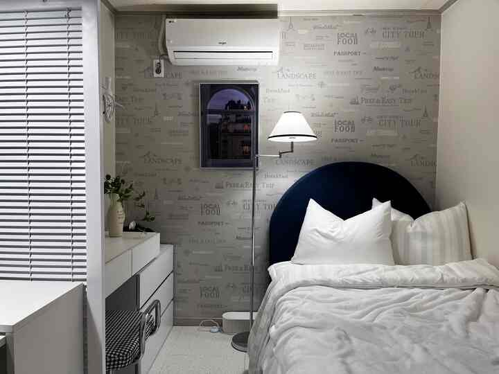 White and navy toned bedroom featuring a navy rounded headboard bed, white bedding, floor lamp, and storage dresser creating a cozy atmosphere