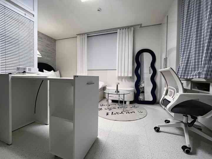 White-toned studio bedroom featuring a folding table and full-length mirror in a simple modern style