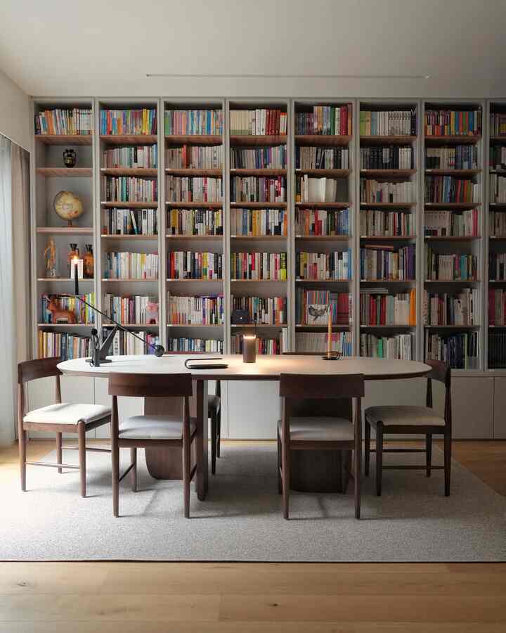 Gray-toned wall and wood-tone furniture blend in a study-style home office featuring wide bookshelves and dining chairs in a neat space