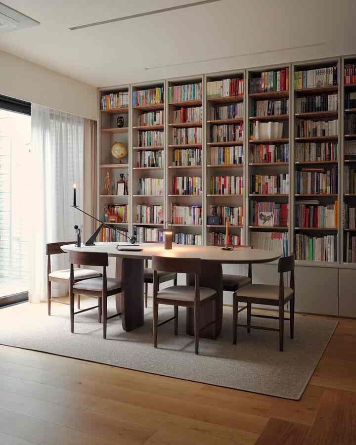 Wood tone and beige study featuring large bookshelves and oval table in a natural modern style space