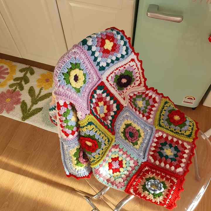 暖かな陽光が差し込む木製フローリングのミニキッチン、花柄の足マットと色とりどりのかぎ針編みのスローが印象的な雰囲気のあるインテリア