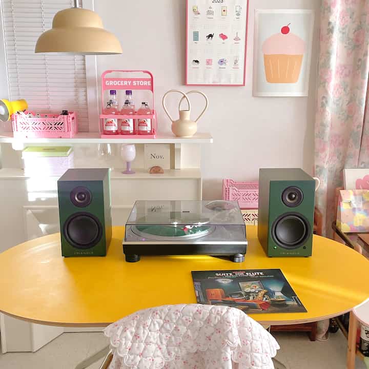 パステル調のかわいらしいホームカフェ空間。黄色のテーブルにレトロなオーディオとピンクの小物が配置された、雰囲気のあるインテリア
