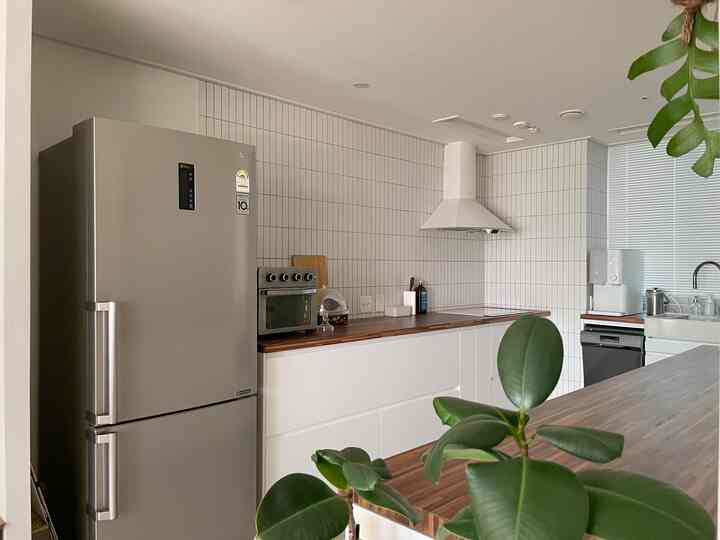 白いタイル壁と木目調カウンターが調和する清潔感のあるイケアキッチン、上部キャビネットなしのミニマルな空間に吊り下げ植物がアクセントを添える