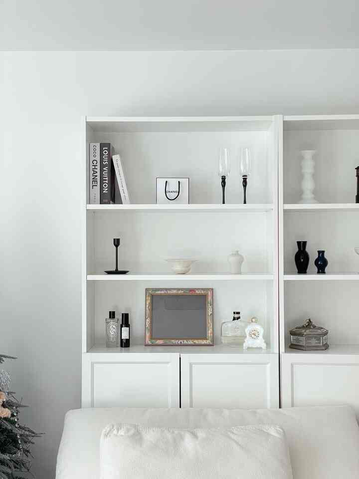 A clean and natural living room in white and ivory tones featuring a central bookshelf and fabric sofa