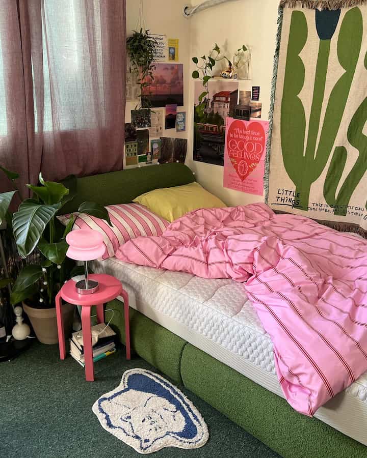 Cozy bedroom with pink duvet cover, green bed frame, plants, and wall posters