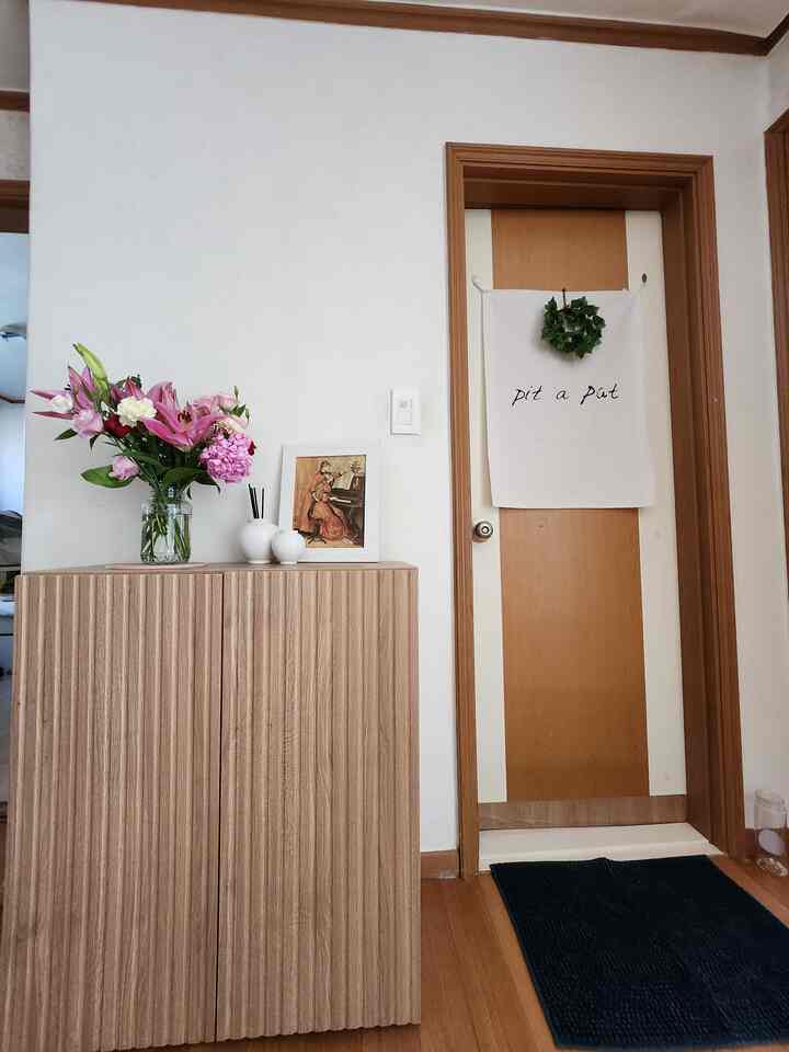 ウッドトーンとホワイトが調和する玄関、収納キャビネットの上に花瓶と額が置かれ、温かみのあるシンプルでナチュラルなインテリア