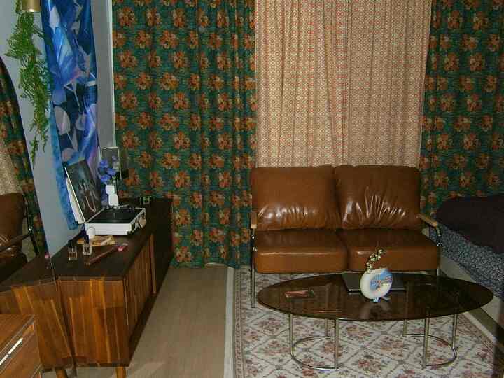 ブラウンの本革ソファとダークグリーンの花柄カーテンが配置されたヴィンテージ風のリビング、木目調の家具と柄入りラグが落ち着いた雰囲気を作り出している