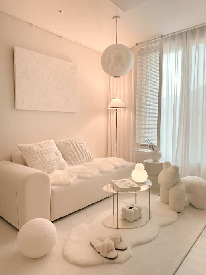 Soft white-toned small living room featuring a large white sofa, wool rug, glass table, and floor lamp creating a cozy atmosphere