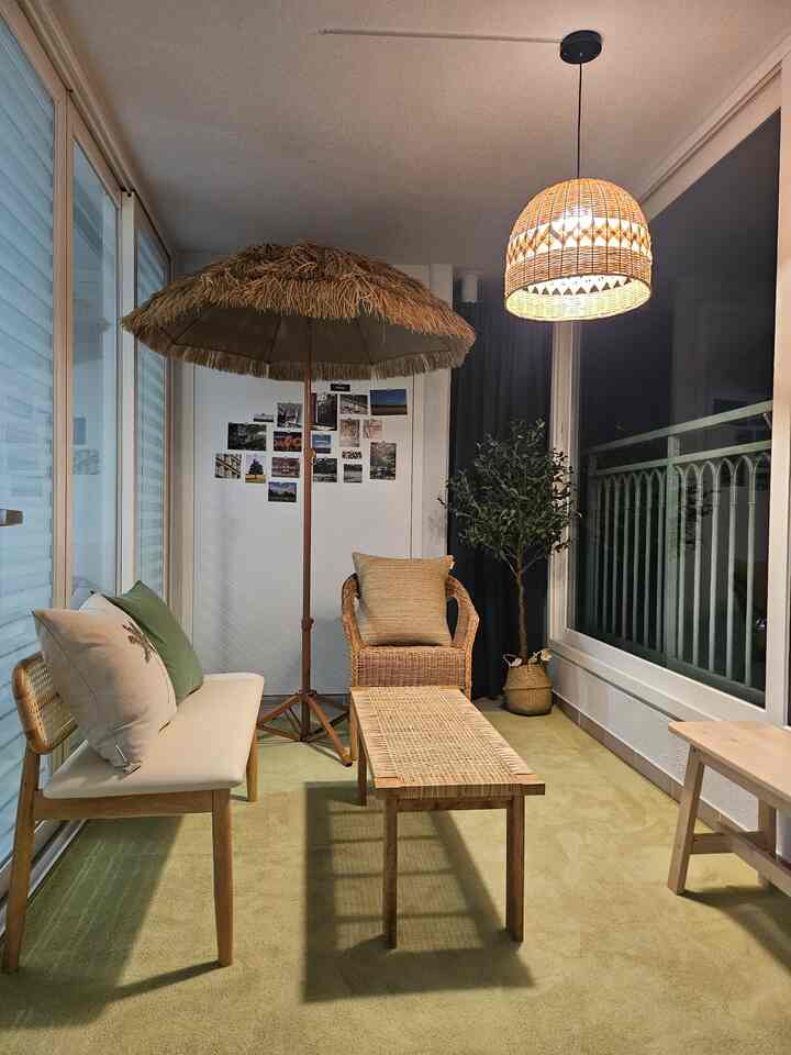 ナチュラルなグリーンカーペットとラタン家具、ラタン照明が配置された居心地の良い広々としたベランダのホームカフェ