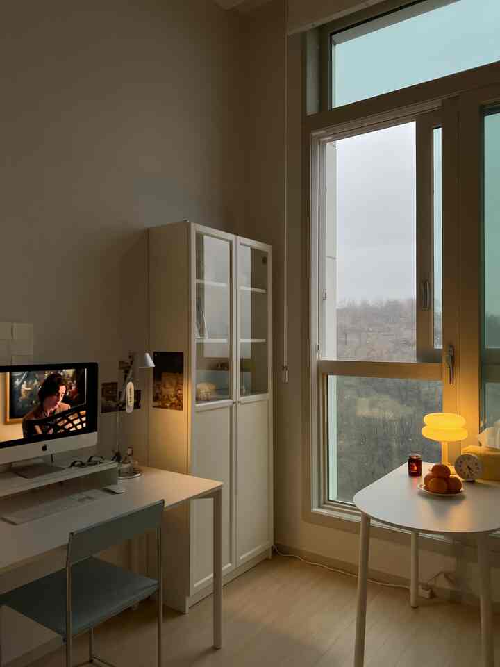 白と自然なトーンのワンルーム、デスクとキャビネットが配置され、大きな窓から自然光が差し込む雰囲気のあるインテリア