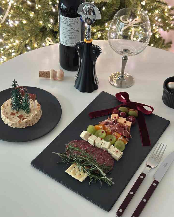 白い丸テーブルにクリスマスツリー形のチーズプラッターとワイン、ワインオープナー、ワイングラスが配置された雰囲気のあるインテリア
