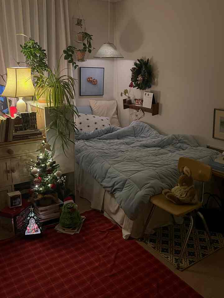 暖かい照明とクリスマス装飾のあるヴィンテージ風ワンルーム寝室、青い寝具と植物が配置された居心地の良い空間