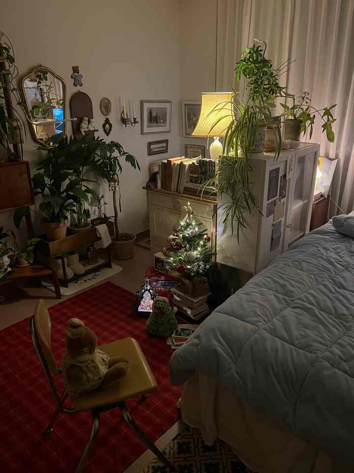 暖かいナチュラルトーンの寝室、ミニクリスマスツリーとヴィンテージ照明、豊かな観葉植物が配置された雰囲気あるインテリア