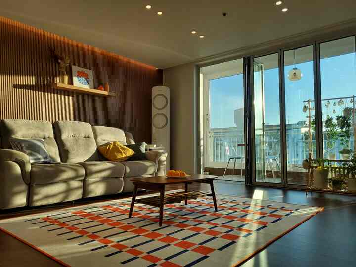 温かみのある木目調の壁とチェック柄ラグが印象的な北欧風リビング、大きなソファと木製コーヒーテーブルが配置された落ち着いた空間