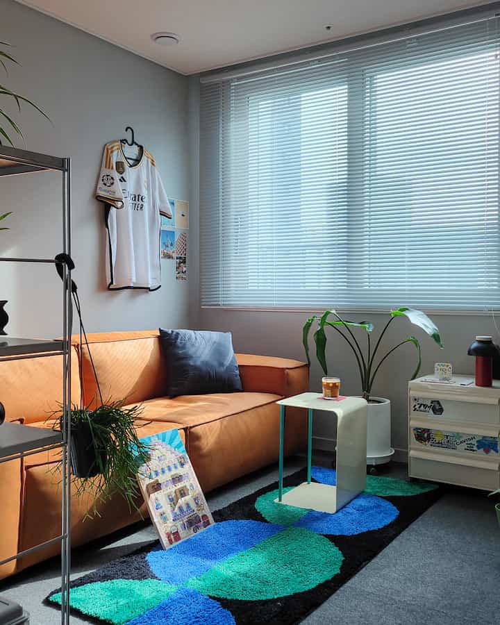 A compact living room with white and orange tones featuring an orange sectional sofa and colorful rug in a cozy media room