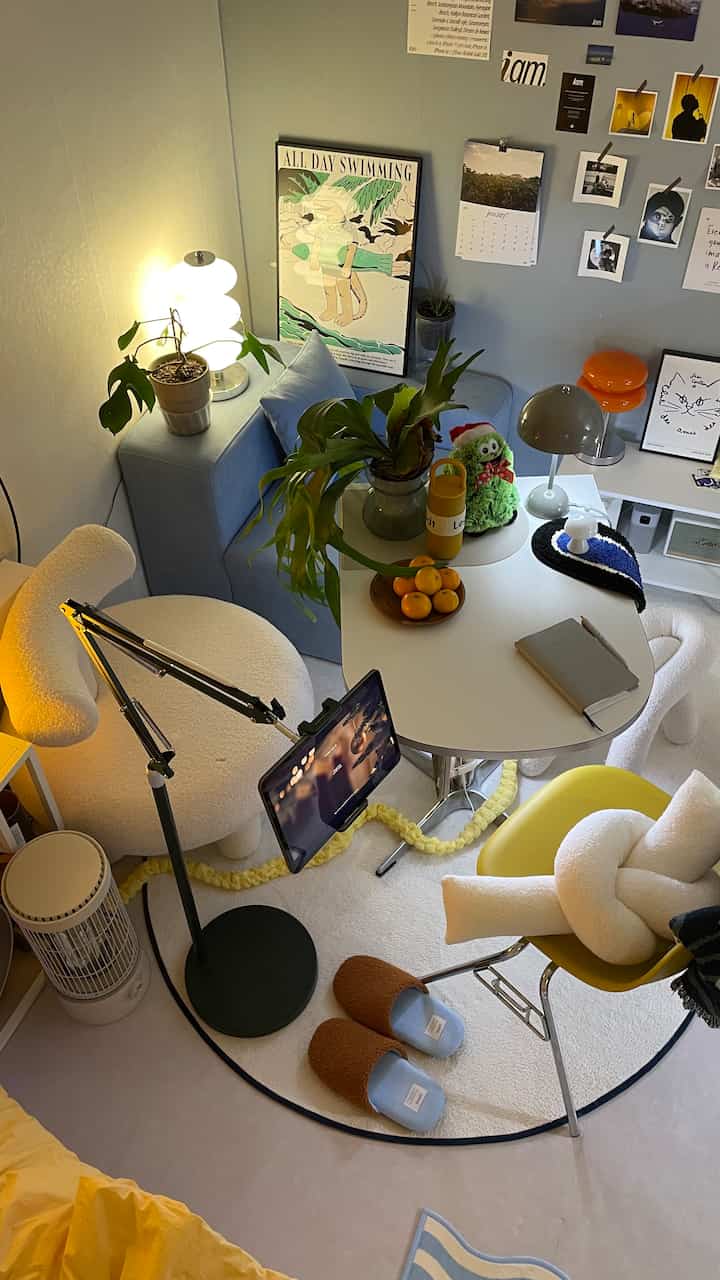 パステルブルーとホワイトのトーンが特徴的なワンルーム、シングルソファと円形テーブル、作業用スタンドライトが配置された居心地の良い空間