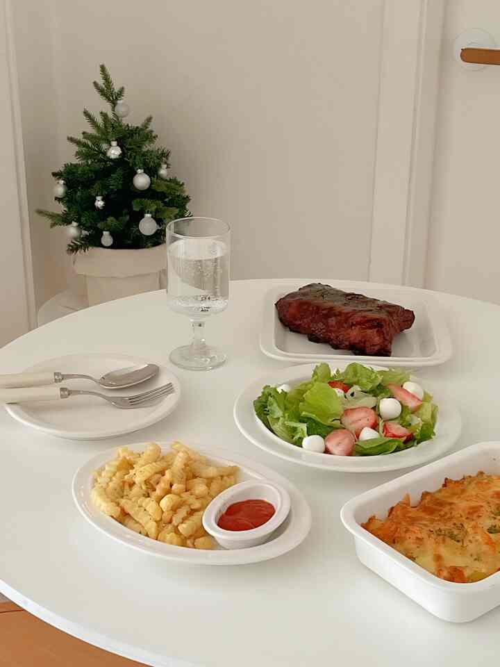 ホワイトトーンのコンパクトなキッチンスペースに、クリスマスの飾りと共にホームパーティー用の皿と料理が並べられた清潔感のあるインテリア