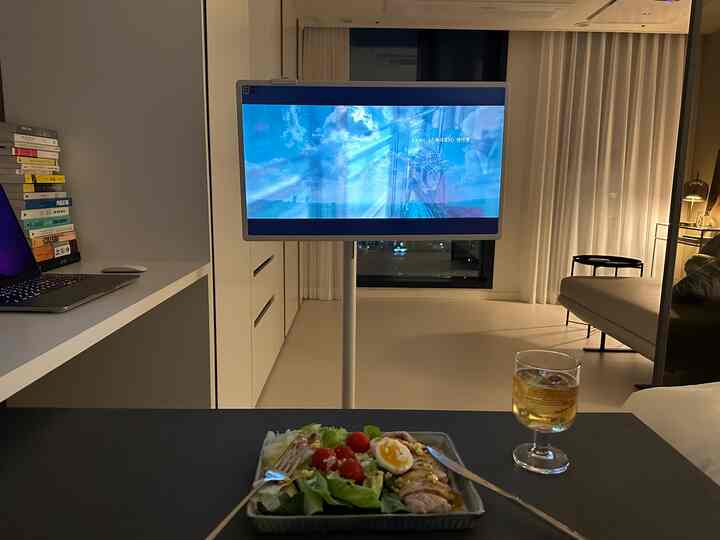 白とベージュのトーンのワンルーム空間、スマートスクリーンテレビとソファが配置されたコンパクトなホームオフィス兼ホームシネマ