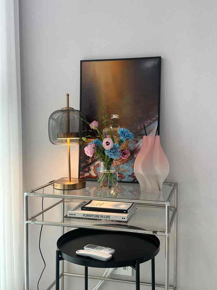 透明なガラステーブルにピンクのディフューザー、花瓶、モダンなテーブルランプが配置されたワンルームのディスプレイスペース