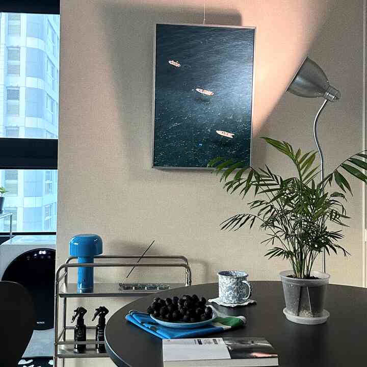 柔らかなベージュの壁とブラックの円形ダイニングテーブルが配置されたワンルーム、植物とポスターが調和した雰囲気のあるインテリア