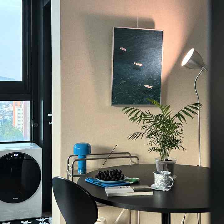 落ち着いたベージュの壁と黒い丸テーブル、植物とフロアランプが配置されたワンルームの印象的なダイニング空間