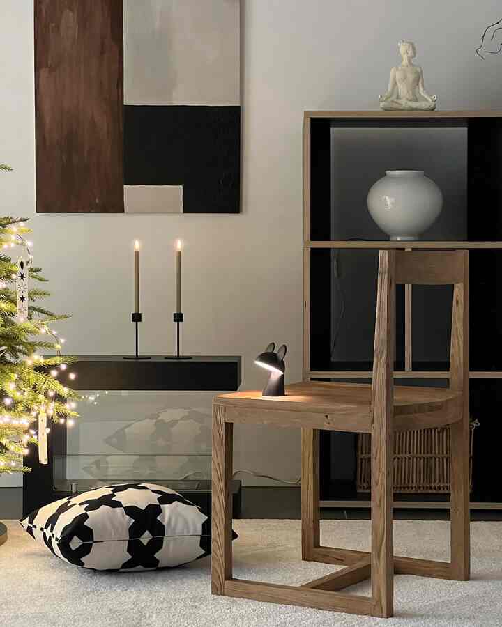 A monotone and wood-toned bedroom space featuring a wooden chair with a character lamp, black-and-white cushion and lit candles in a simple interior design