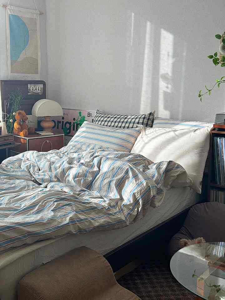 温かみのあるベージュとブルーが調和するワンルーム寝室、快適な寝具と木製家具、ペット用ビーンバッグが配置された雰囲気あるインテリア