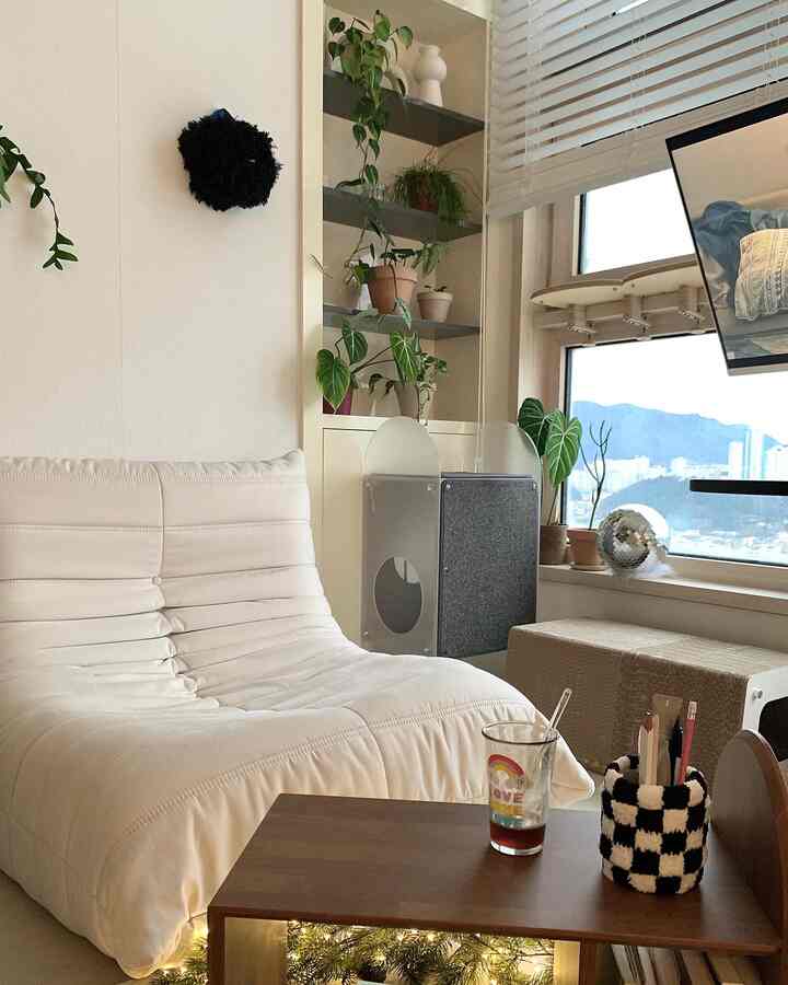 Bright white-toned living room with cream sofa and wooden coffee table, cozy space featuring a cat tower and plants by the window
