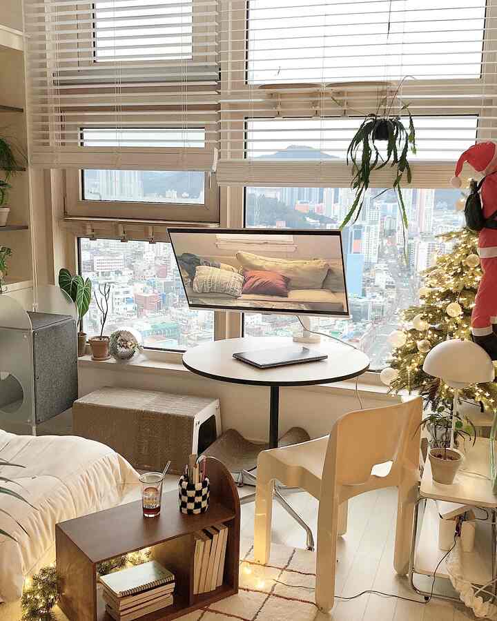 Bright white and beige living room featuring a round white table, side table, Christmas tree, and a cat scratching post, creating a cozy home party atmosphere
