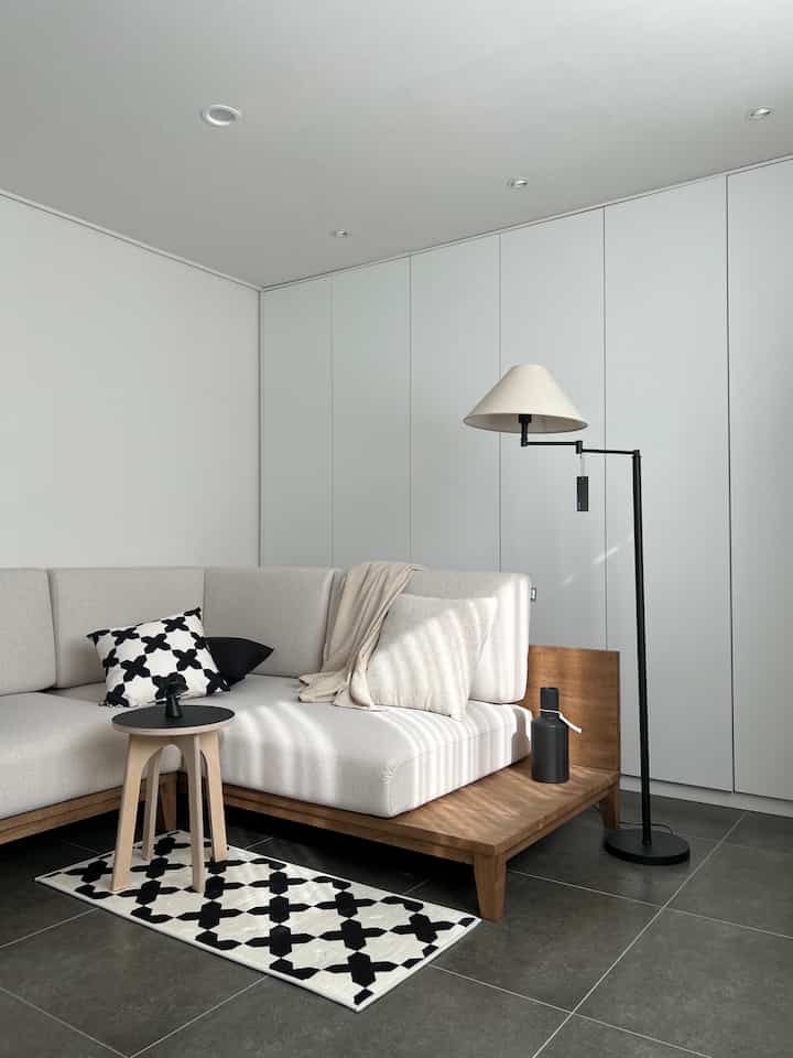 A beige and wood-toned mini living room featuring a fabric sofa and floor lamp in a simple, cozy setting