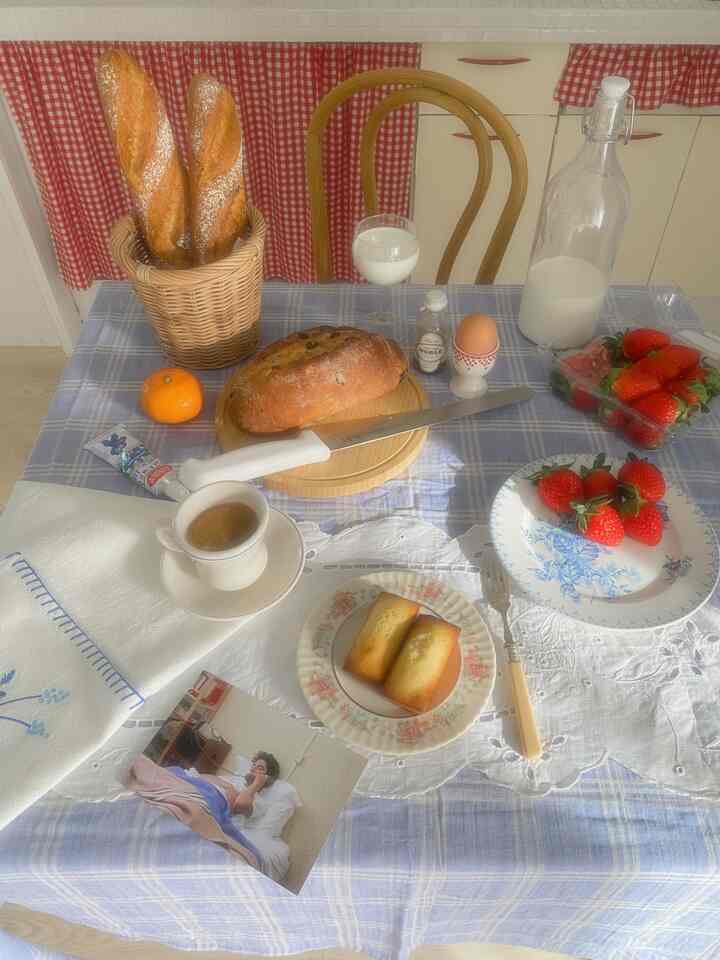 ブルーとホワイトの色調のキッチン、ヴィンテージのテーブルクロスにパンや牛乳、イチゴが置かれた雰囲気のあるブランチテーブル