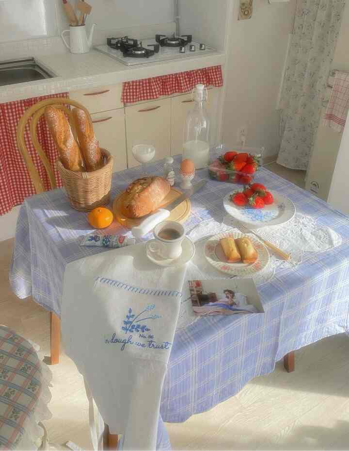 白とナチュラルカラーのキッチン、チェック柄テーブルクロスの上にパンや果物、コーヒーが置かれた雰囲気のあるブランチテーブル