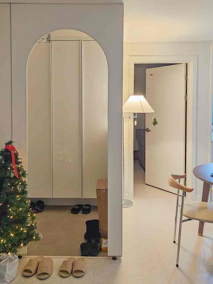 白と茶色のトーンの玄関、アーチ型パーティションとクリスマスツリーが配置された清潔感と温かみのあるインテリア