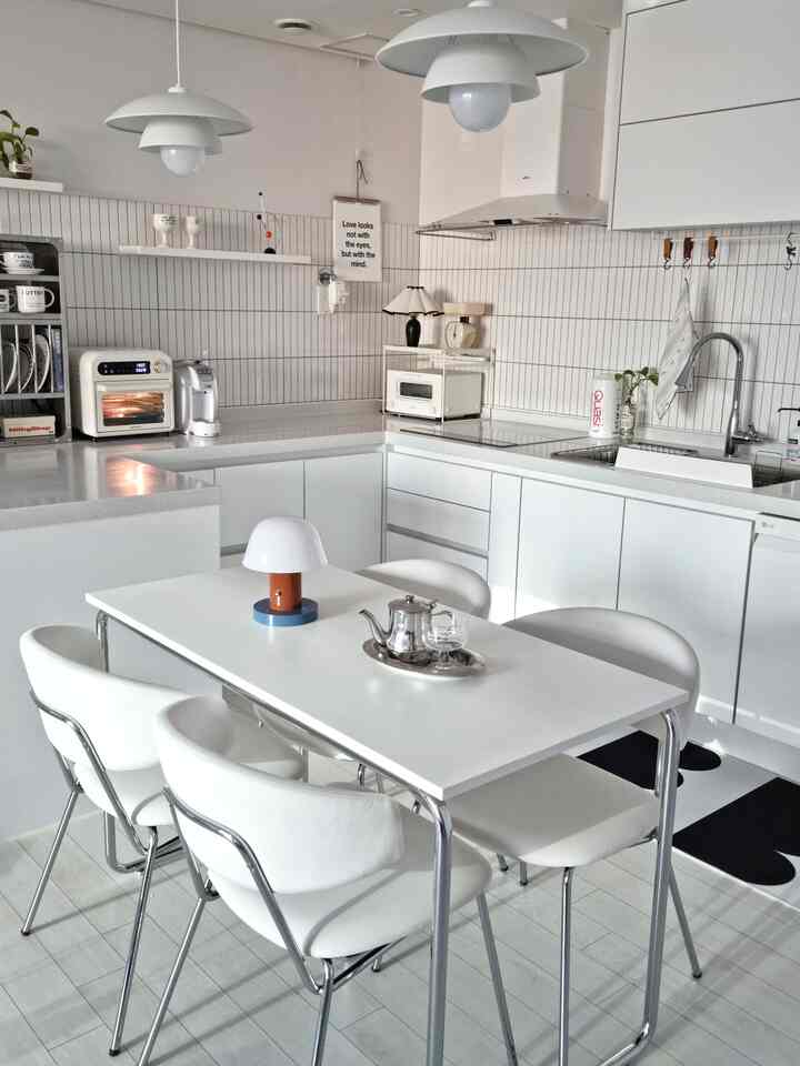 Clean white-toned kitchen space featuring mid-century modern dining table and pendant lights with a sleek, modern aesthetic