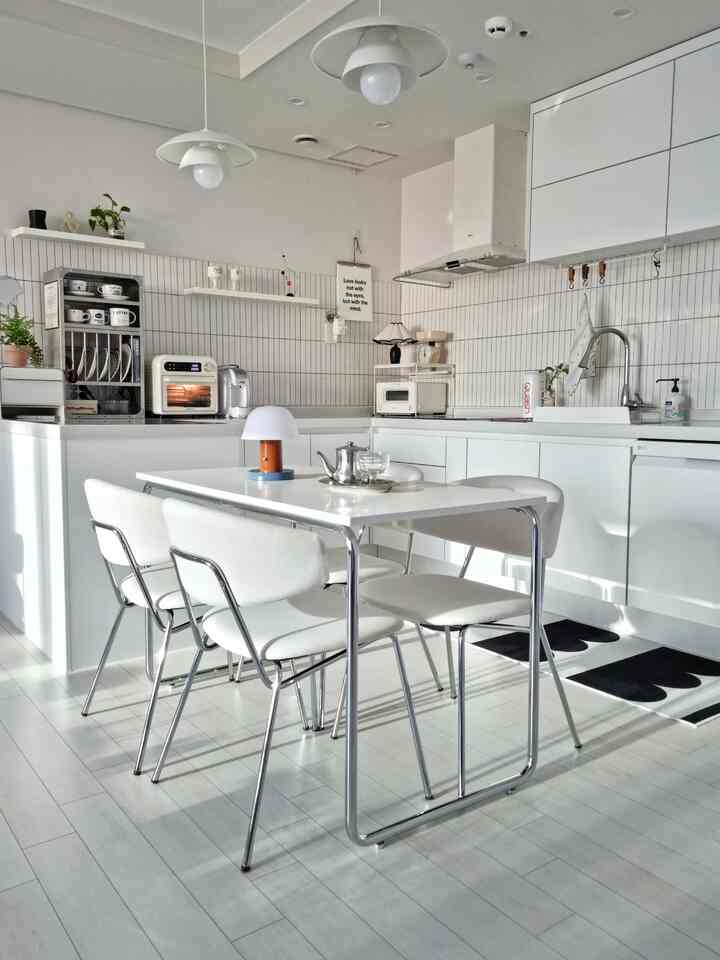 白を基調としたキッチン、ミッドセンチュリーモダンのダイニングテーブルと椅子が配置された清潔感のあるモダンな空間