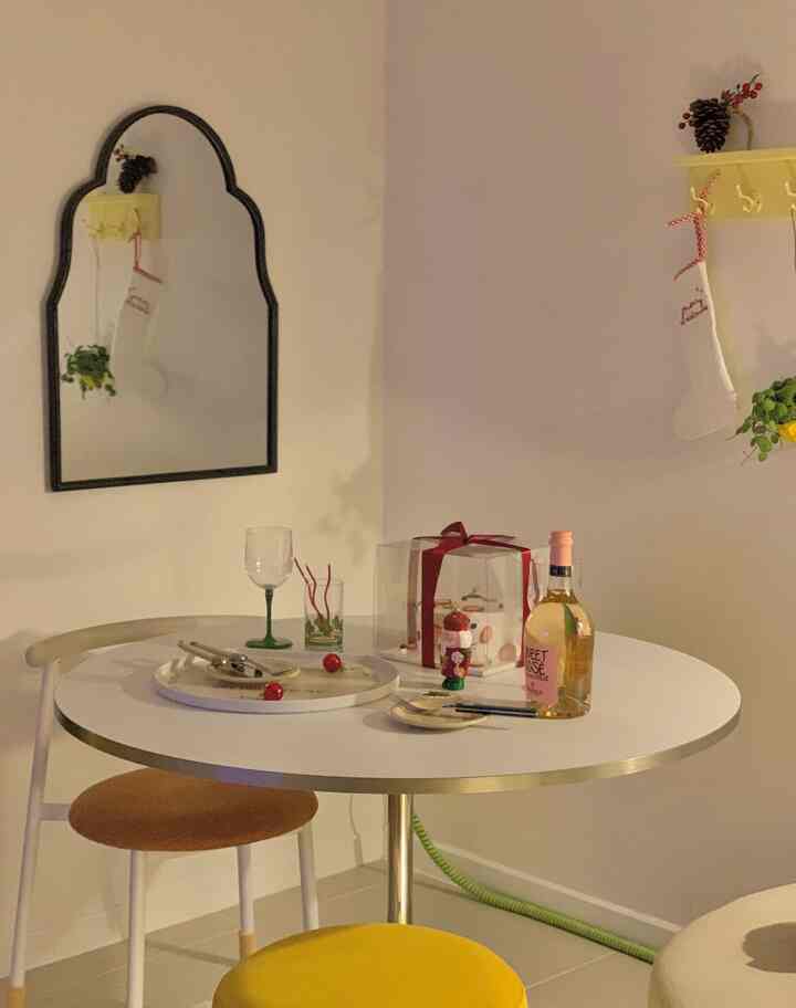 White-toned living area featuring a round white dining table with gold-edged chairs decorated for a Christmas home party