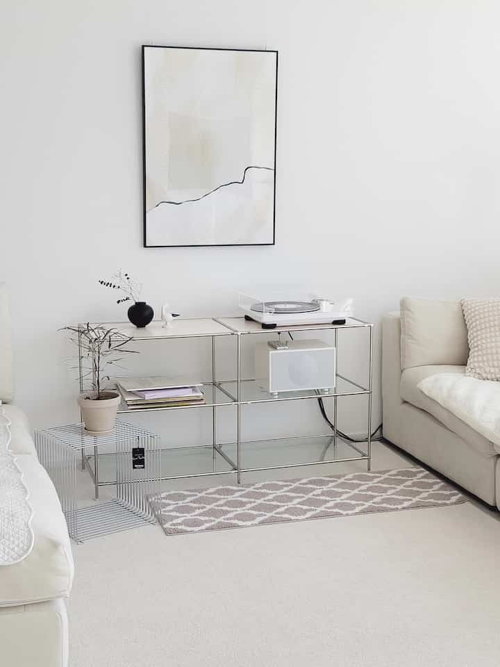 A white-dominant living room featuring cream sofas and a metal framed shelf with a clean, minimalistic interior style