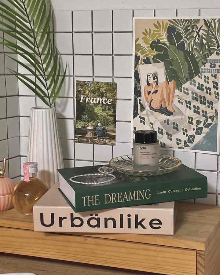 Natural veranda interior featuring white tiled wall and wooden shelf with artwork, fake books, plant, and plate decor items