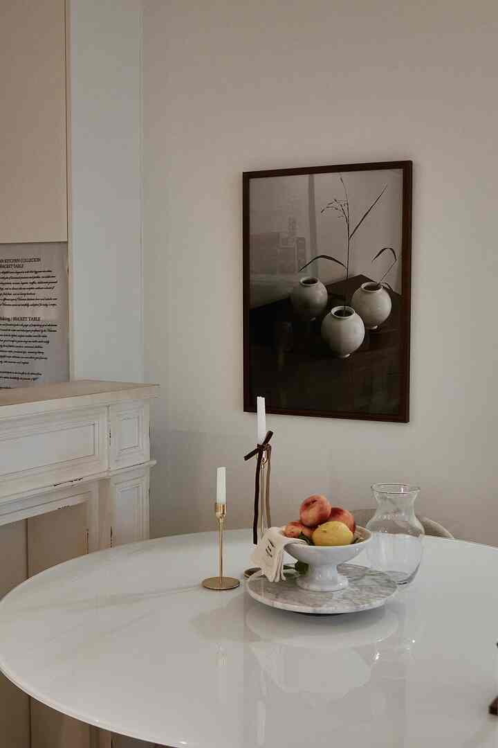 White-toned dining room featuring a round table with gold candle holders and a vintage picture frame creating a simple year-end atmosphere