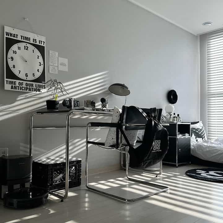 Modern home office and bedroom with black and white furniture and decor, featuring sleek desk and armchair