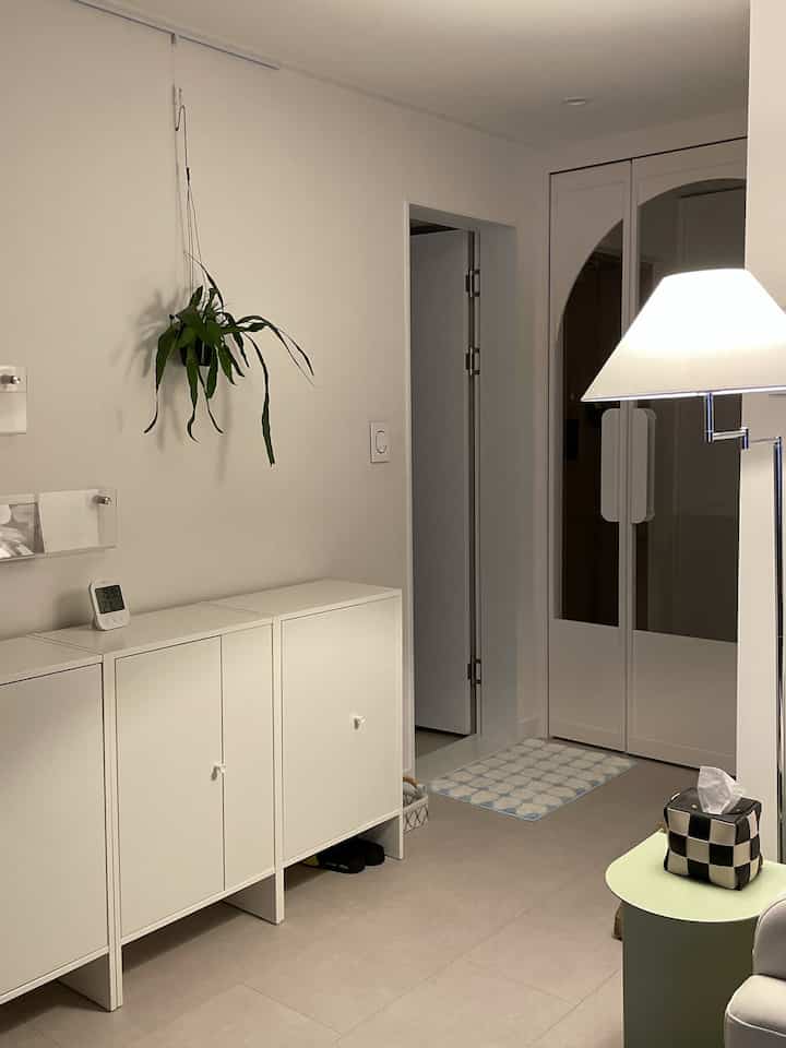 白を基調とした玄関の廊下、狭い隙間に設置された白い収納家具と壁にはハンギングプラントが配置された雰囲気のあるインテリア