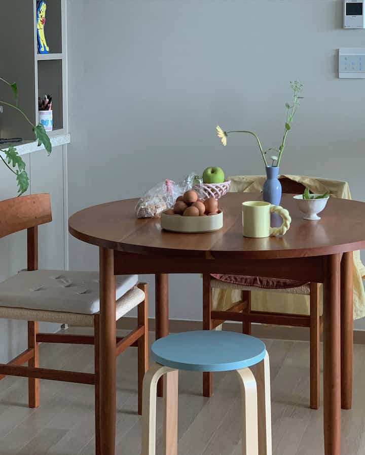 Natural and simple dining room with beige walls and a wooden round dining table featuring ceramic bowls and a vase on the table
