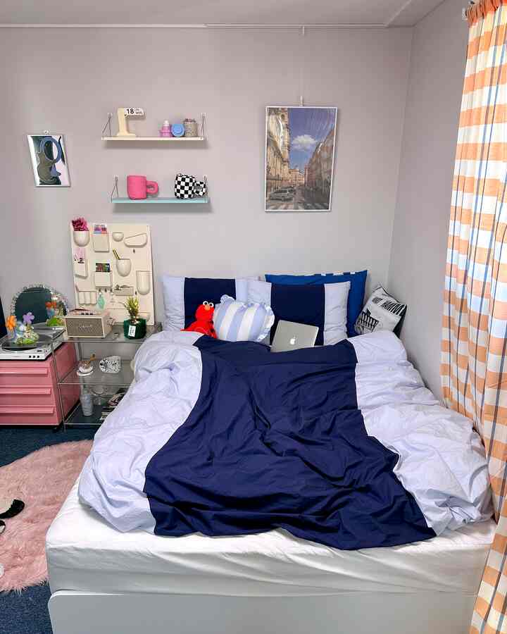 ネイビーとホワイトのトーンの寝室、整った寝具と黄色ストライプのカーテンが配された雰囲気のある空間