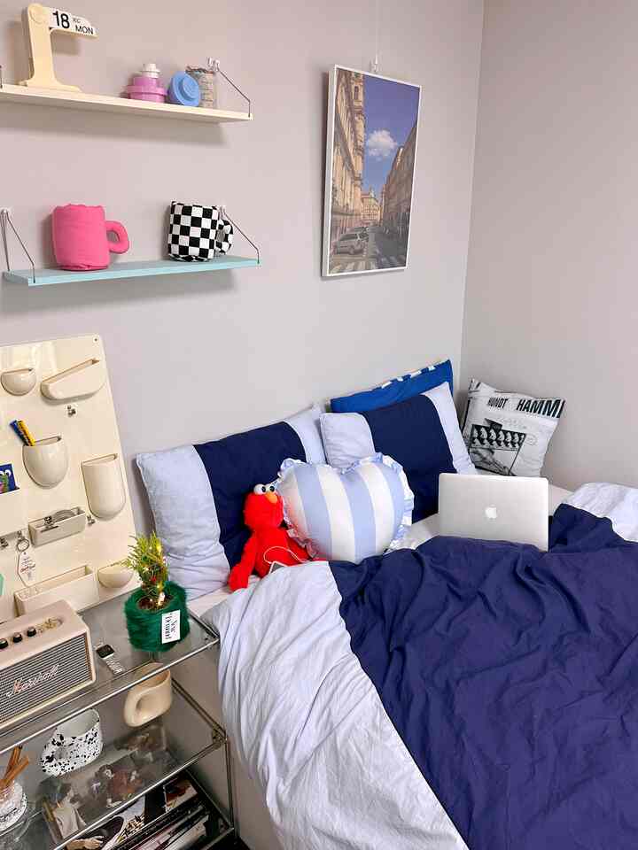 ホワイトとネイビーカラーの狭い寝室、壁棚と多様なクッションが配置された雰囲気のある個人空間