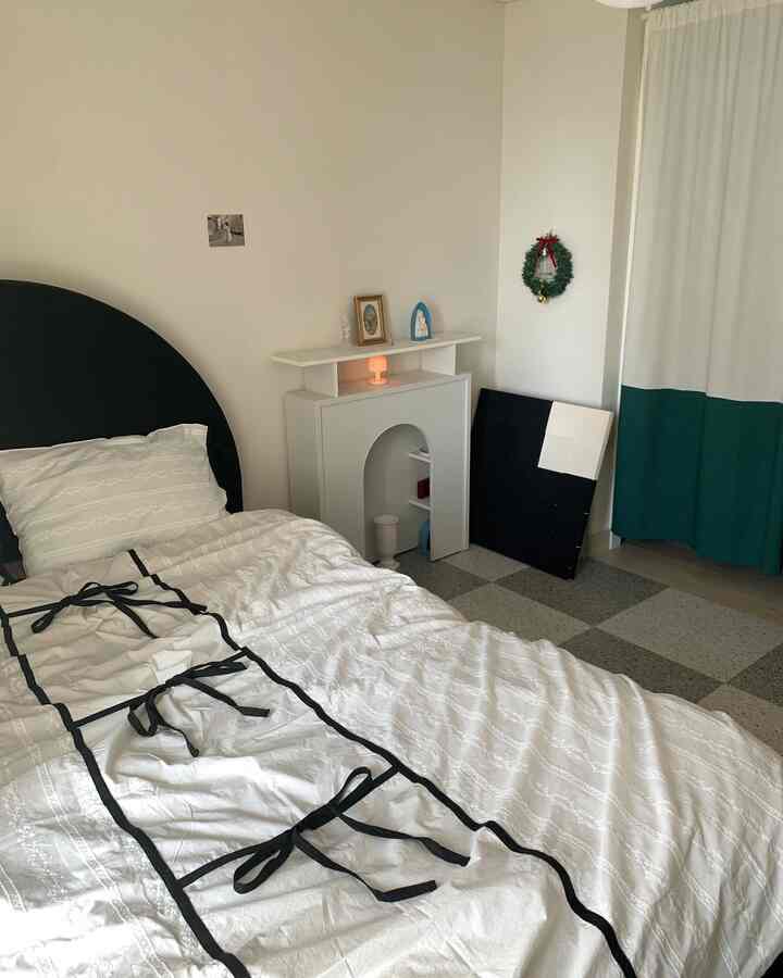 白と緑のトーンが印象的な寝室、ベッドとアーチ型の暖炉風棚、カーテンが配置された雰囲気のあるインテリア