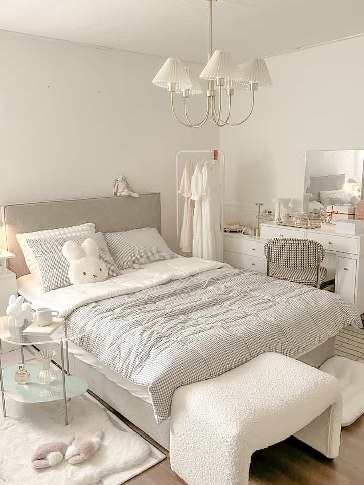 Bright white and beige bedroom featuring a gray bed with checked bedding, vanity table, and a patterned chair in a cozy atmosphere