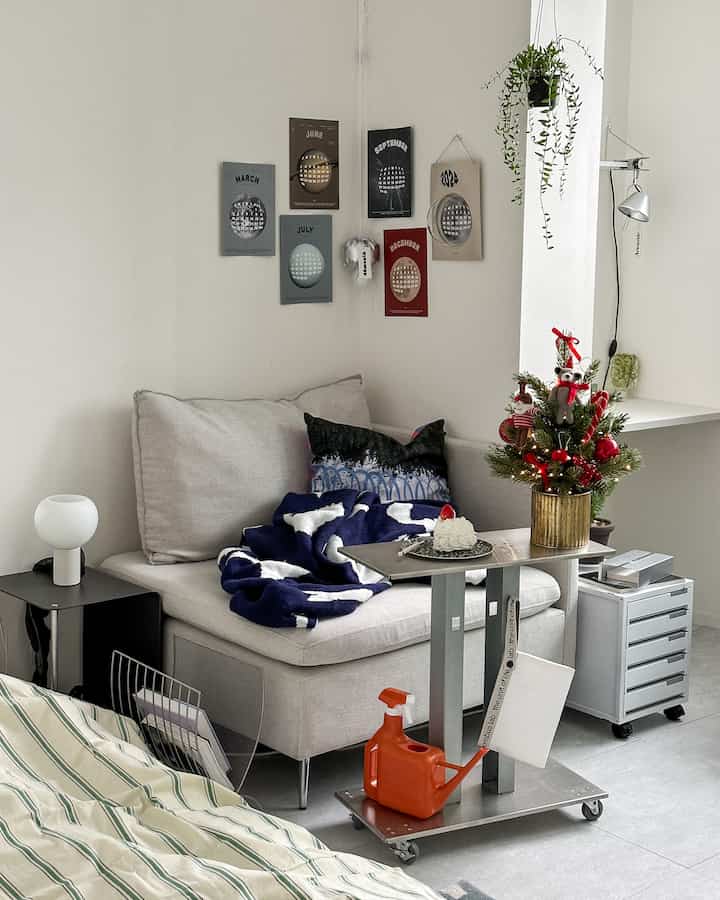 A cozy small living room in white and navy tones featuring a sofa bed, table lamp, and Christmas decorations