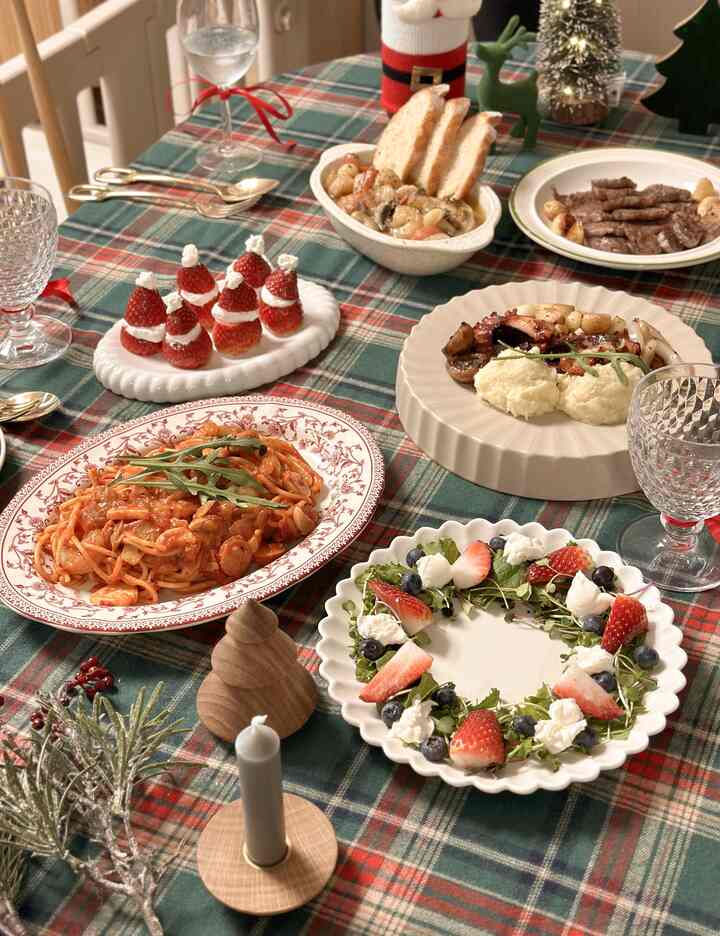 Cozy Christmas home party dining table with green plaid tablecloth, decorated plates, and festive ornaments centrally arranged
